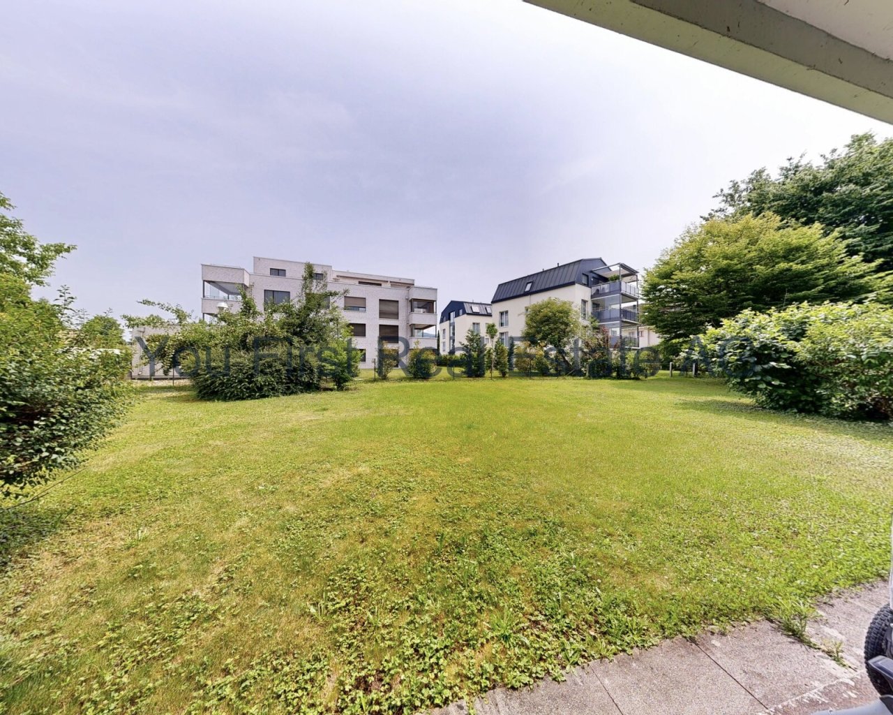 Großzügiger Gemeinschaftsgarten mit moderner Wohnanlage im Hintergrund